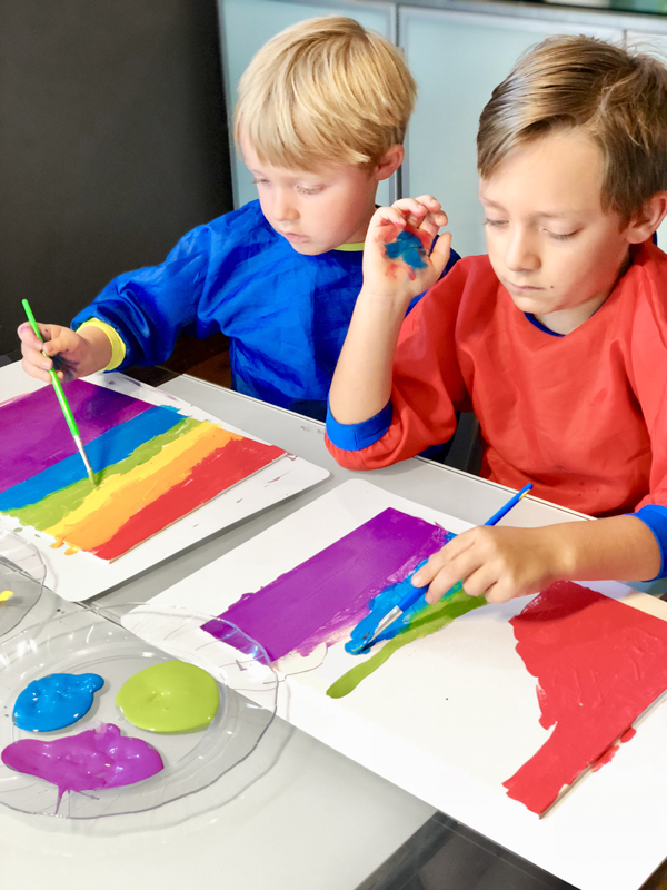 Kids painting rainbow stripes on canvas