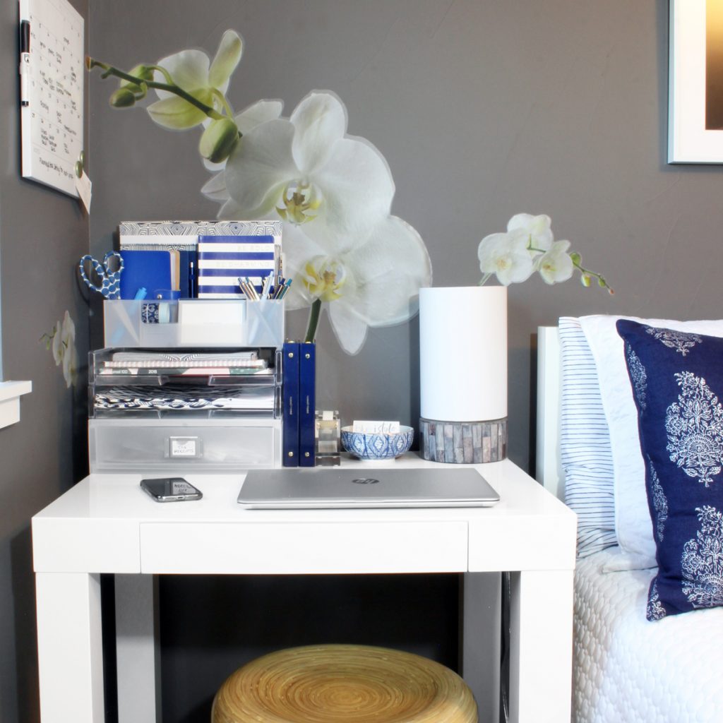 White writing desk in place of nightstand in guest room with dark gray walls