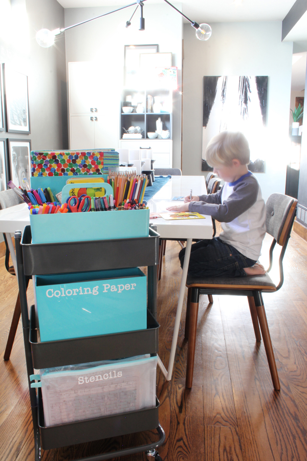 Little boy drawing at kitchen table with rolling art cart next to him