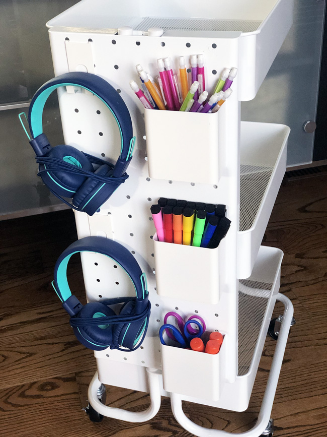 Pegboard on a rolling cart with hooks for headphones and cups filled with pencils and markers