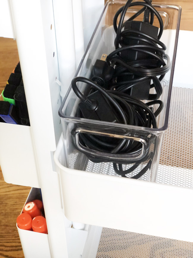 Computer chargers in clear bin on second shelf of rolling cart